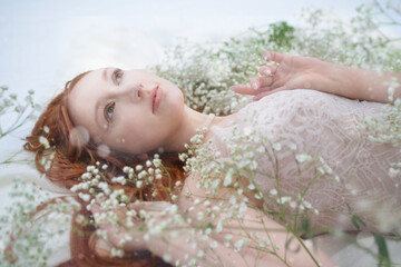Red-haired woman in the snow among small white flowers
