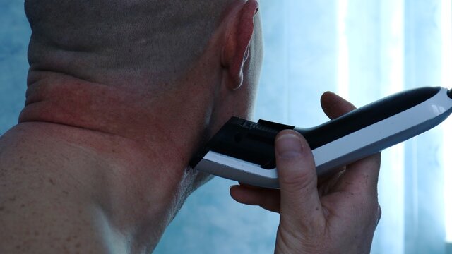 Thorough Self-shaving Of The Stubble On A Man's Neck At Home With An Electric Hair Clipper In The Blue Neon Lighting Of The Bathroom, Partially Visible Shaved Head And Muscular Neck Of The Person