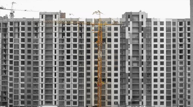 A tower crane is being dismantled into sections against the backdrop of a new building. Jib crane vertical disassembling 4k