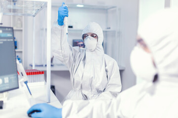 Lab scientist in healthcare lab holding micropipette with sample dressed in ppe suit against...