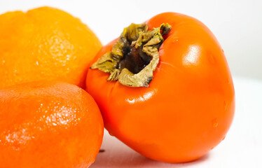 A whole ripe persimmon, with a tangerine and an orange lying next to it.
