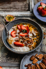 oatmeal with fresh berries, nuts and passionfruit sauce in blue bawl on shabby beige background, healthy breakfast concept