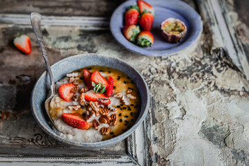 oatmeal with fresh berries, nuts and passionfruit sauce in blue bawl on shabby beige background, healthy breakfast concept