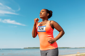 fitness, sport and race concept - young african american woman running marathon with badge number on shirt