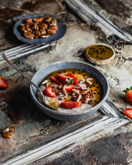 oatmeal with fresh berries, nuts and passionfruit sauce in blue bawl on shabby beige background, healthy breakfast concept