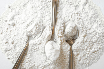Tablespoons in loose flour on the table. Minimalism, pure white. Background for screensaver or desktop.