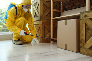 Pest control worker in protective suit spraying pesticide indoors
