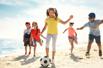Cute children playing soccer at beach on sunny day. Summer camp