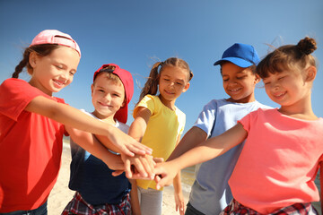 Group of children putting hands together outdoors on sunny day. Summer camp