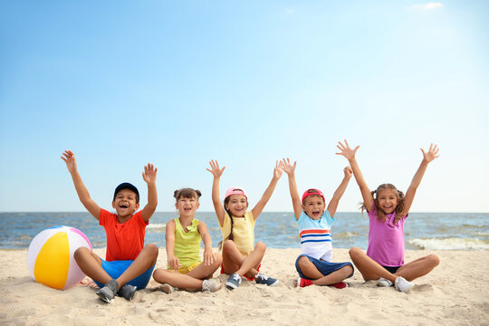 Group of happy children sitting on sand at sea beach. Summer camp