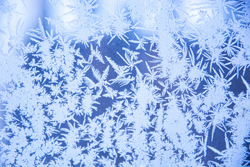 Snowy frosty pattern on a glass surface. Frost on the glass of the window. Frosty window. Snowflakes on the glass in winter. Winter morning outside the window. Background.