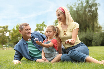 Naklejka na ściany i meble Happy family blowing soap bubbles in park on green grass