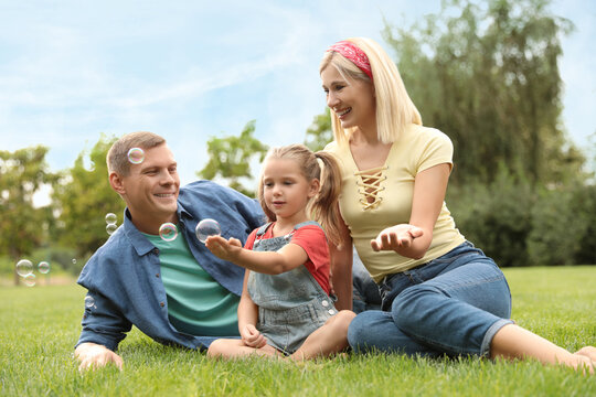 Happy family blowing soap bubbles in park on green grass