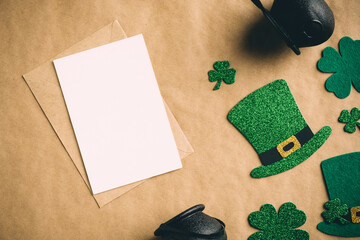 Happy St Patrick's Day concept. Vintage flat lay composition with blank greeting card mockup, leprechaun hats, clover shamrock leaves, pots of gold on kraft paper background.