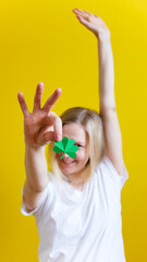 Shamrock in hand of young women in front of her face. Girl's face on yellow background. Selective focus.