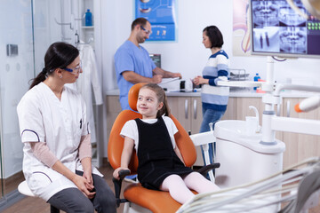 Little girl waiting for professional dental hygine examining looking at dentist doctor. Child with her mother during teeth check up with stomatolog sitting on chair.