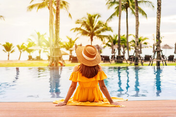 Young woman traveler relaxing and enjoying the sunset by a tropical resort pool while traveling for summer vacation - obrazy, fototapety, plakaty