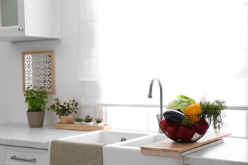 Basket full of different vegetables on wooden board in modern kitchen