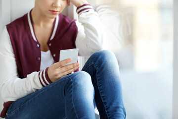 sadness and people concept - sad teenage girl with smartphone sitting on window sill