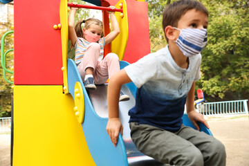 Fototapeta na wymiar Little children with medical face masks on playground during covid-19 quarantine