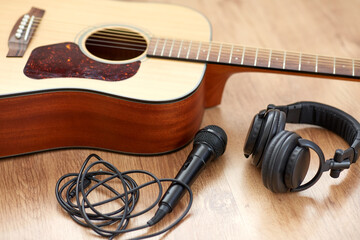 leisure, music and musical instruments concept - close up of acoustic guitar, microphone and headphones on black table