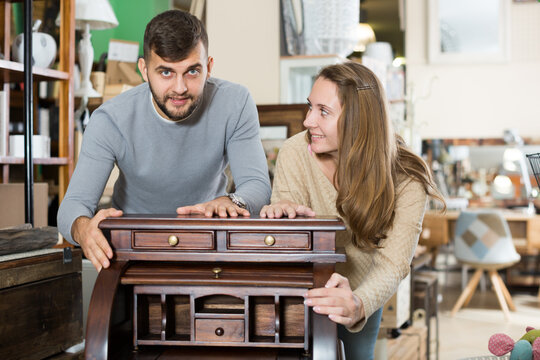 Happy girl with boyfriend choosing vintage cabinet in furnishings store