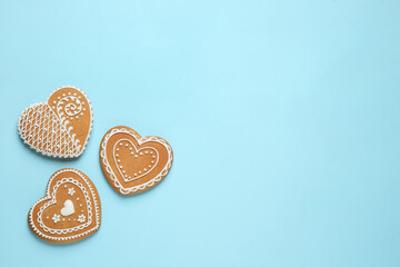 Gingerbread hearts decorated with icing on light blue background, flat lay. Space for text