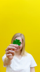 Shamrock in hand of young women in front of her face. Girl's face on yellow background. Selective focus.