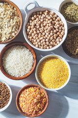 Flat lay of dry cereals and legumes in white and wooden bowls, white background. Vegan protein concept.
