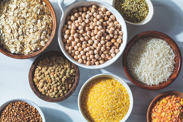 Flat lay of dry cereals, grains and legumes in white and wooden bowls, white background. Vegan protein concept.