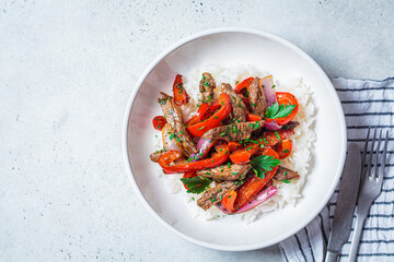 Fried pieces of beef with vegetables and rice in white plate. Stir fry beef with peppers and onions, served with rice.