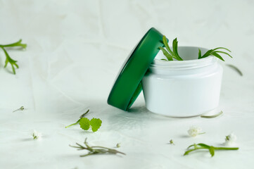 open white jar of cream with leaves and plants on a light background. Natural lighting selective focus