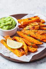 Sweet potato fries with guacamole on wooden plate, gray background. Vegan food concept.