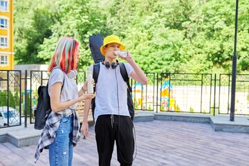 Cheerful talking students teenagers guy and girl in city drinking milk yogurt from bottle