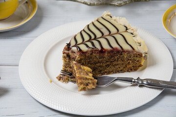 Very tasty piece of cake cut with a fork on a white plate and a cup of coffee in yellow on a light wooden table. The process of eating cake and enjoying sweet foods