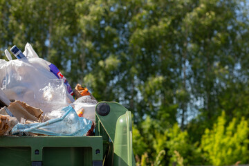 An overflowing trash can on a forest background. Human concept harming the ecology of the planet,...
