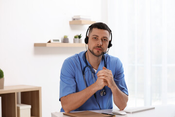 Fototapeta premium Doctor with headset sitting at desk in clinic. Health service hotline
