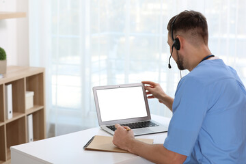 Doctor with headset consulting patient online at desk in clinic, space for text. Health service hotline