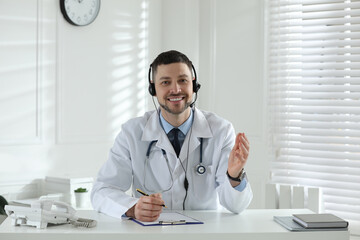 Doctor with headset consulting patient over phone at desk in clinic. Health service hotline