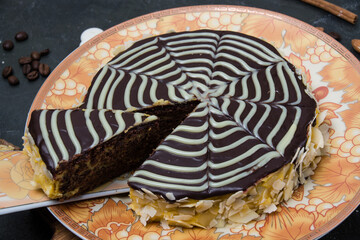 Chocolate sliced esterhazy cake with cream, frosting, nuts and almonds close-up on an orange-brown plate on a dark concrete background
