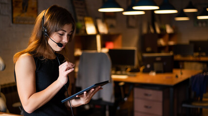 Beautiful caucasian woman in a headset is holding a digital tablet. Portrait of a business woman in the office