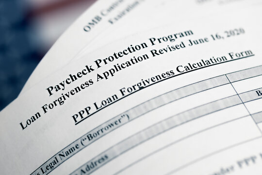 selective focus photo of paycheck protection program loan forgiveness application form revised, on a background of United States flag. paycheck protection program new round.