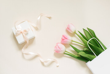 Bouquet of delicate tulips and a white box gift with a bow on an beige background, floral festive arrangement of flowers