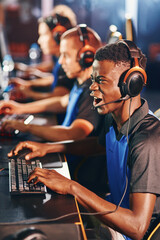 Enjoyment. Side view of a young excited african guy, male cybersport gamer wearing headphones playing online video games while participating with in eSport tournament - obrazy, fototapety, plakaty