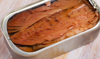 Appetizing natural frigate mackerel fillets in open tin can on wooden table ..