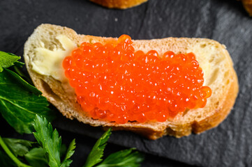 Red caviar in bowl and Sandwiches on stone board. Black background. Top view