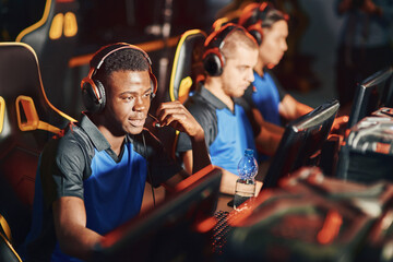 Professional cybersport gamer wearing headphones talking by microphone with team member while playing online video game. eSport tournament concept