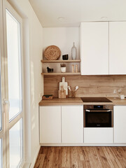 Stylish boho home kitchen interior concept. Wooden shelfs, dishes, utensils, vases, decorations. Cozy white comfortable interior design.