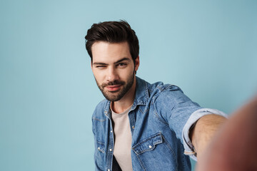 Obraz premium Young handsome pleased man winking while taking selfie photo