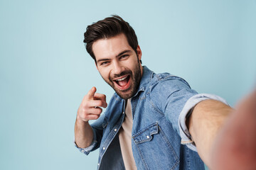Young excited man pointing finger at camera while taking selfie photo